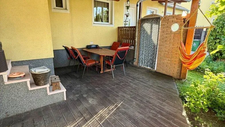 Überdachte Holzterrasse mit Esstisch und Hängematte, umgeben von grüner Bepflanzung.