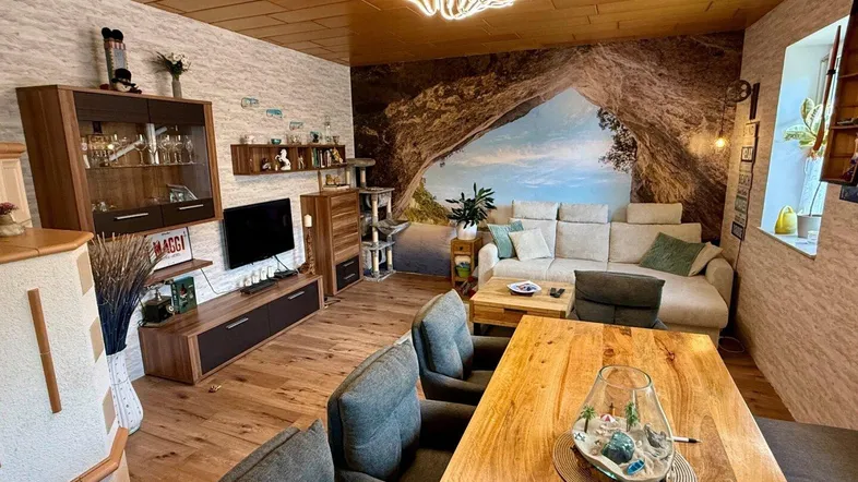 Gemütlicher Wohn-Essbereich mit Holzboden, großem Esstisch und einer modernen Couch.