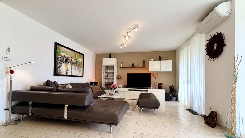 Geräumiges Wohnzimmer mit Klimaanlage, großem Sofa und Zugang zum Balkon.