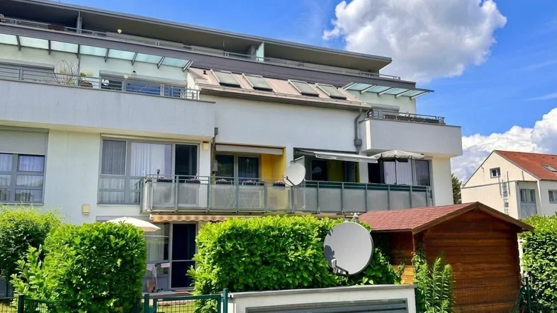 Modernes Mehrfamilienhaus mit mehreren Balkonen und einem gepflegten Vorgarten unter blauem Himmel.