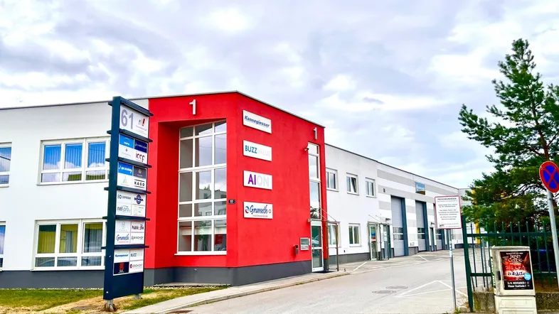 Modernes Geschäftsgebäude mit roter und weißer Fassade sowie großen Fenstern und Beschilderung.