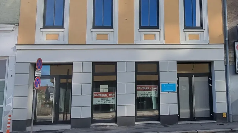 Fassade eines Geschäftsgebäudes mit großen Schaufenstern und darüberliegenden Wohnungen.