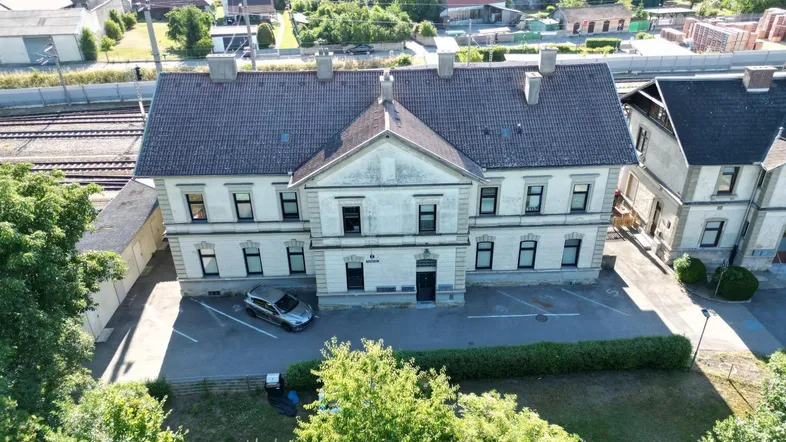 Draufsicht auf zwei ältere Gebäude mit Satteldächern, umgeben von Bäumen und einem Parkplatz.