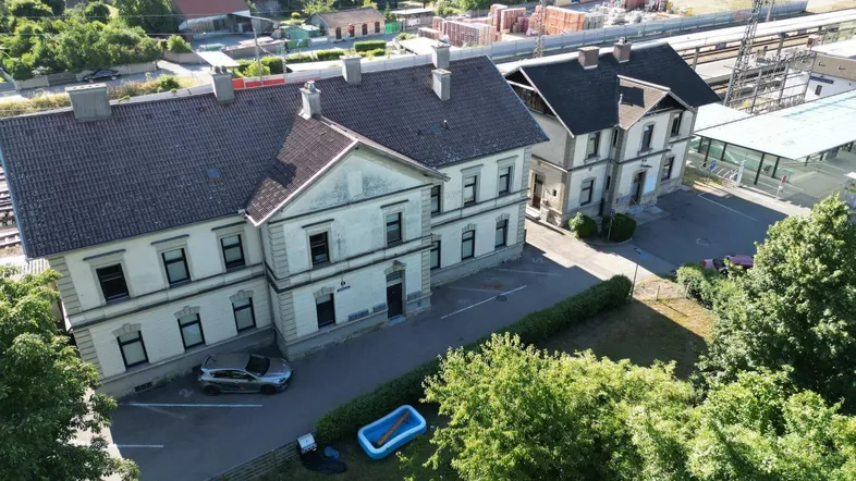 Luftaufnahme zeigt zwei historische Gebäude mit Parkplätzen und viel Grün in ländlicher Umgebung.