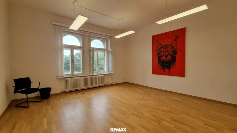 Heller Raum mit Holzboden, großen Fenstern und einem auffälligen roten Kunstwerk an der Wand.