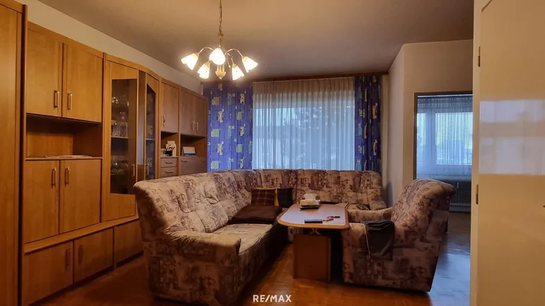 Gemütliches Wohnzimmer mit großem Ecksofa, Holzmöbeln und Vorhängen in Blautönen.