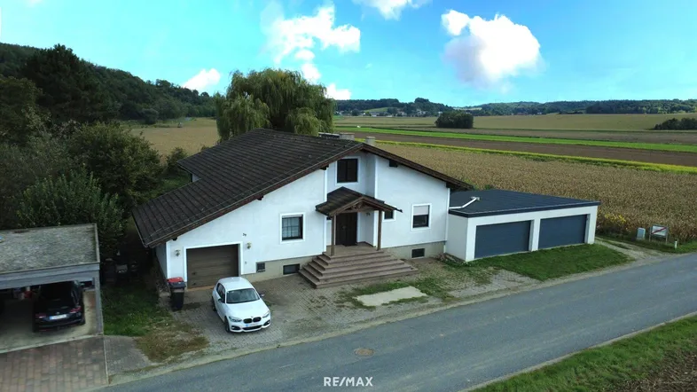 Freistehendes Einfamilienhaus mit Doppelgarage und Carport, umgeben von Feldern und Natur.