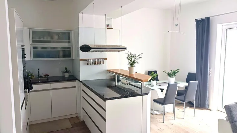 Moderne offene Küche mit dunkler Arbeitsplatte, integriertem Essbereich und hellem Parkettboden.