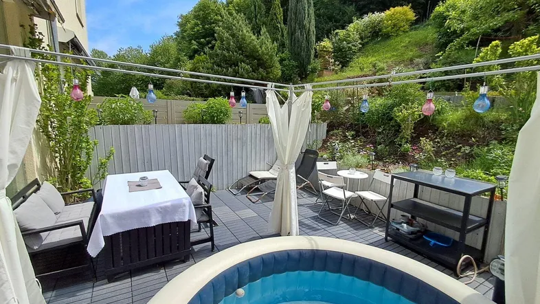 Geräumige Terrasse mit Whirlpool, Essbereich und Liegestühlen, umgeben von viel Grün.