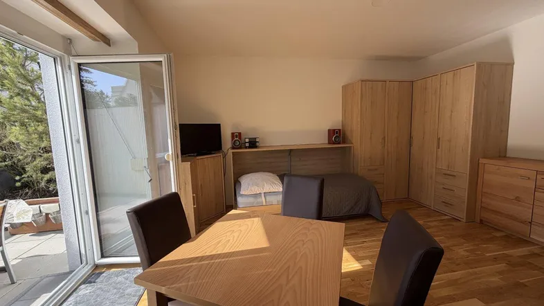 Helles Zimmer mit Parkettboden, Esstisch und Zugang zu einer sonnigen Terrasse.