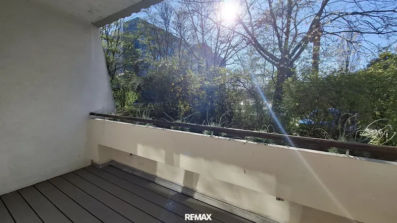 Sonniger Balkon mit Holzboden und Blick ins Grüne sowie auf die umliegenden Berge.