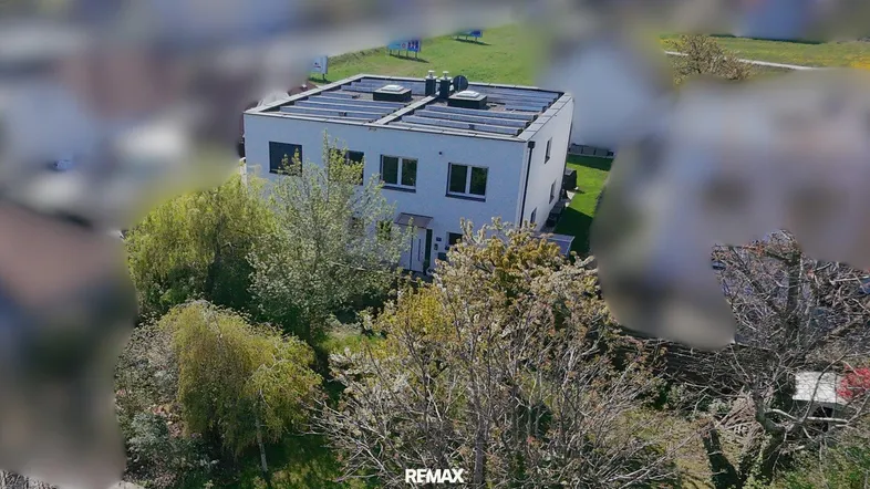 Luftaufnahme eines modernen Hauses mit Flachdach und Photovoltaikanlage in grüner Umgebung.