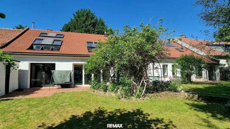Hinteransicht des Hauses mit großem Garten, Terrasse und Dachfenstern, umgeben von viel Grün.
