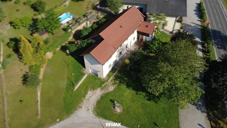 Luftaufnahme eines Hauses mit rotem Ziegeldach, umgeben von viel Grün und einem kleinen Pool.