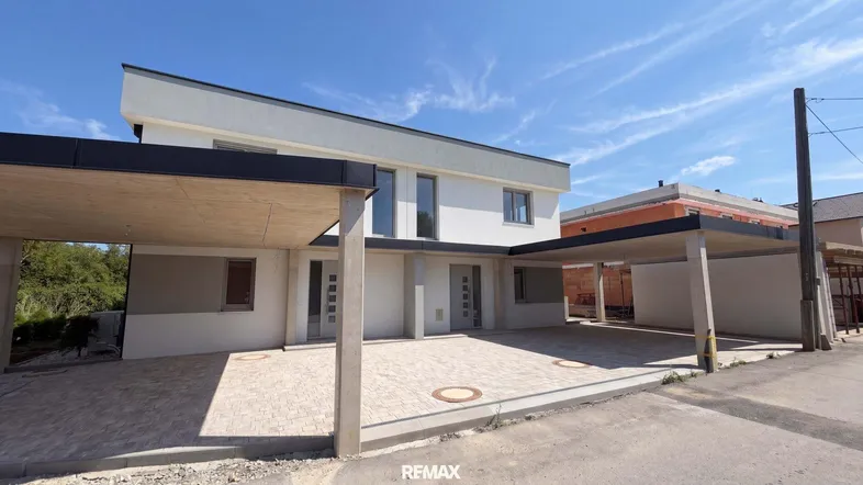 Modernes Reihenhaus mit Carports und gepflastertem Vorplatz unter blauem Himmel.