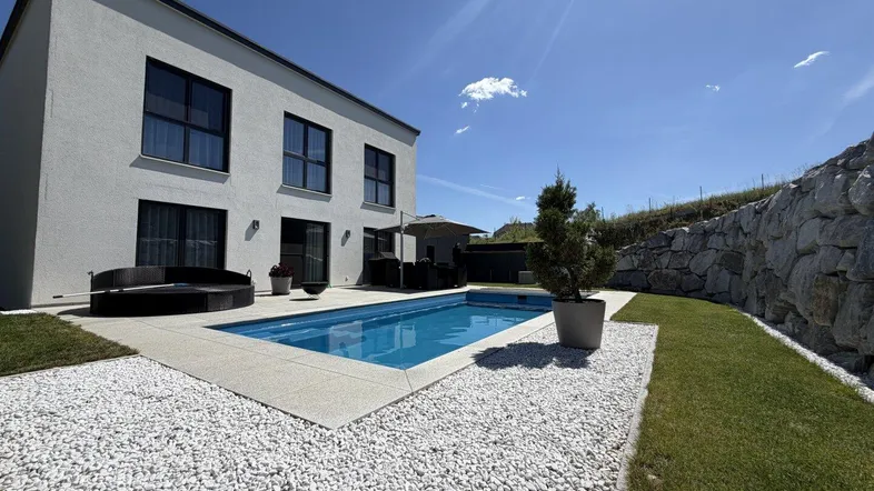 Modernes Haus mit privatem Pool, Whirlpool und gepflegtem Gartenbereich unter blauem Himmel.