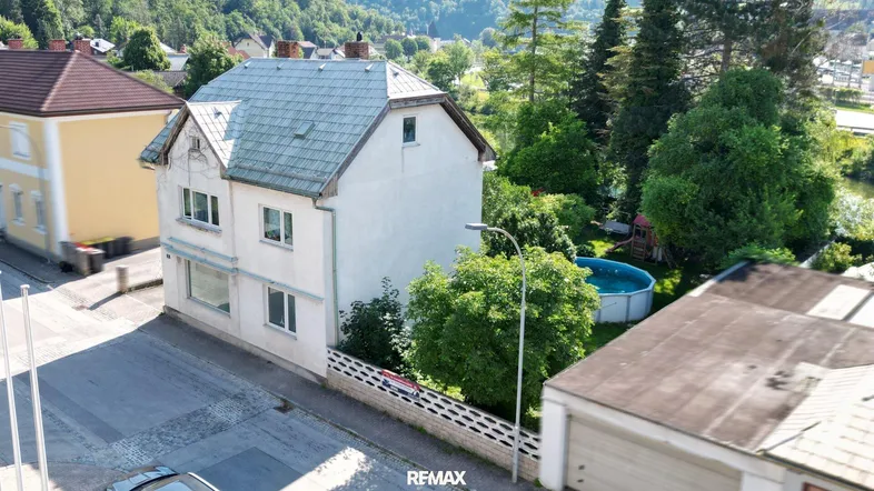 Luftaufnahme eines Einfamilienhauses mit Garten, Pool und umliegender grüner Landschaft.