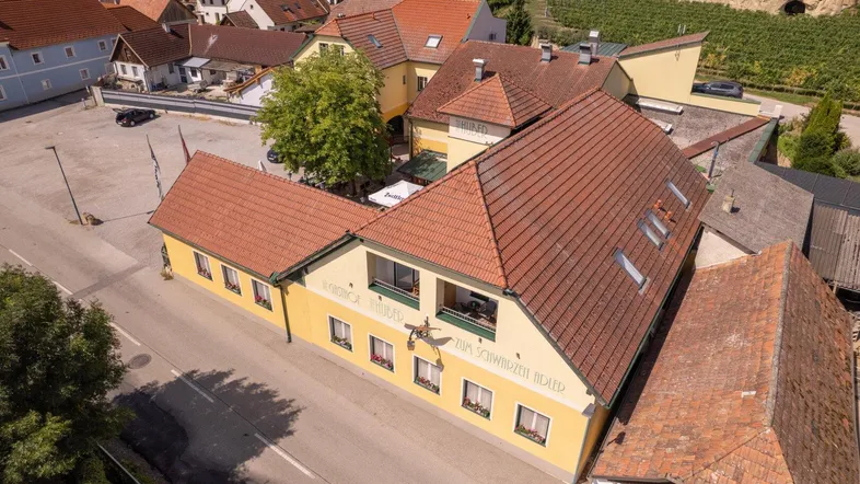 Luftaufnahme des Gasthofs mit traditioneller Architektur, roten Ziegeldächern und umliegender Landschaft.
