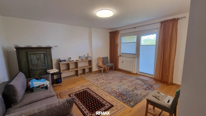 Helles Wohnzimmer mit Holzboden, Teppichen und Zugang zum Balkon.