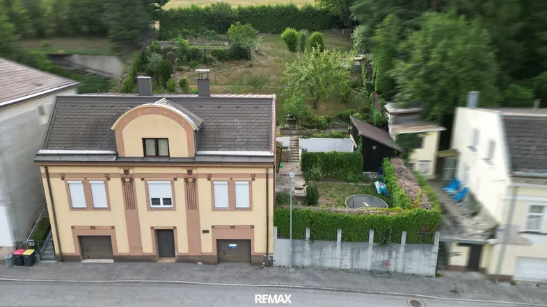 Luftaufnahme eines gelben Hauses mit angrenzendem Garten und umliegender grüner Landschaft.