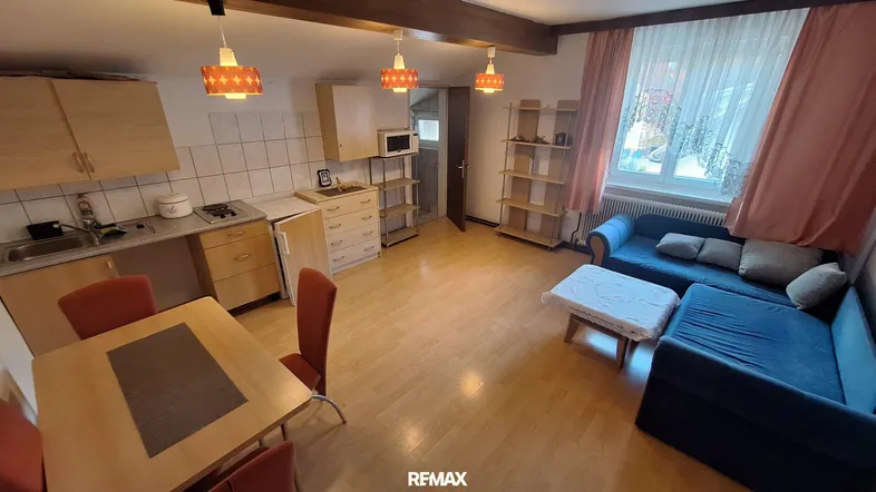 Gemütlicher offener Wohnbereich mit integrierter Küche, Essplatz und Sofa, hell durch großes Fenster.