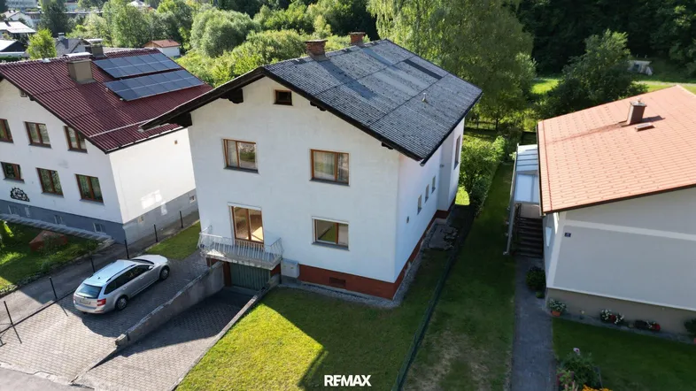 Luftaufnahme eines Einfamilienhauses mit Satteldach, Garten und angrenzenden Gebäuden in grüner Umgebung.