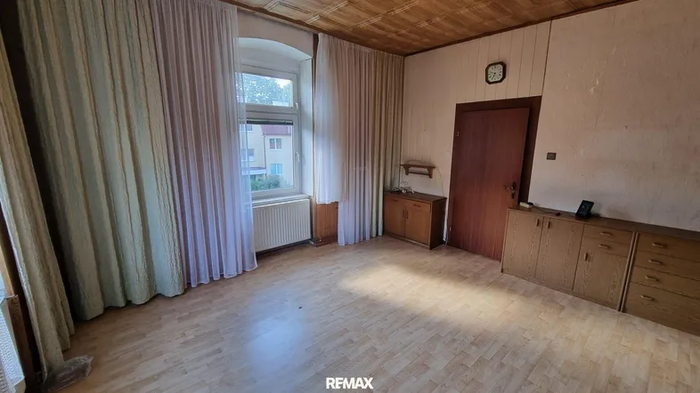 Heller Wohnraum mit Holzdecke, Parkettboden und großem Fenster.