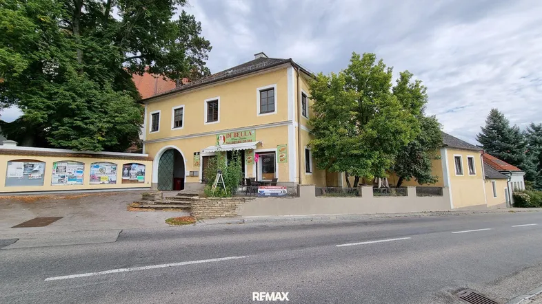 Gelbes Gebäude mit traditioneller Architektur, einer Pizzeria im Erdgeschoss und einer Straße davor.