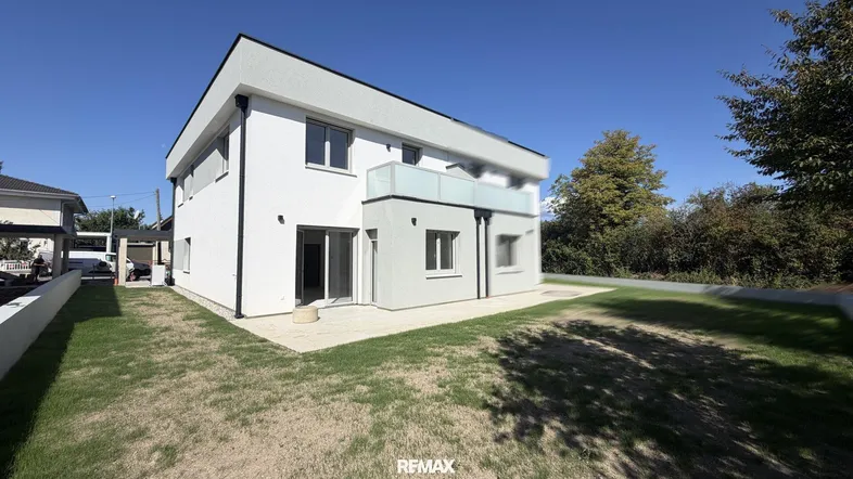 Modernes Einfamilienhaus mit weißer Fassade, Flachdach und kleinem Gartenbereich.