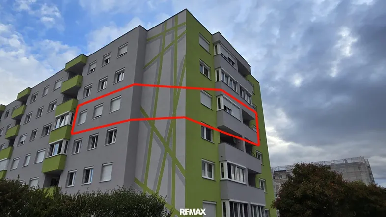 Modernes Mehrfamilienhaus mit auffälliger grau-grüner Fassade und Balkonen unter bewölktem Himmel.