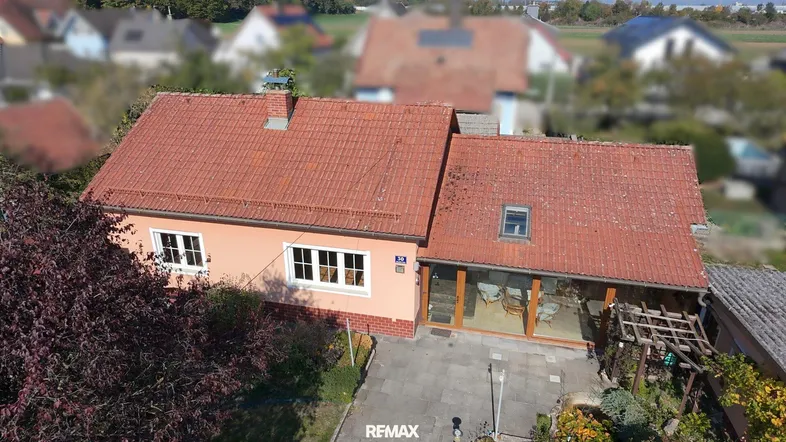 Luftaufnahme eines Einfamilienhauses mit rotem Ziegeldach, Wintergarten und gepflegtem Gartenbereich.