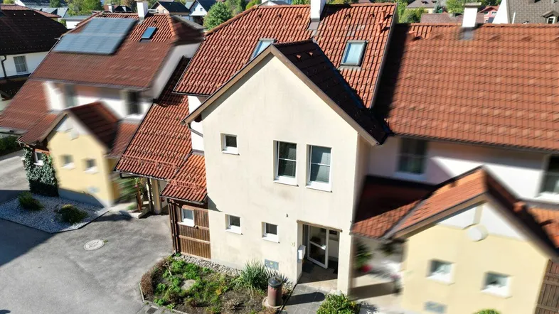 Luftaufnahme eines Reihenhauses mit rotem Ziegeldach und grüner Umgebung.