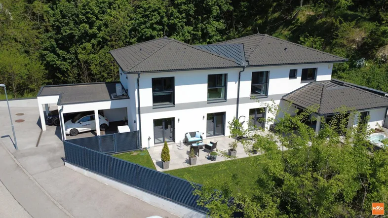Modernes Einfamilienhaus mit weißer Fassade, dunklem Dach und gepflegtem Gartenbereich.