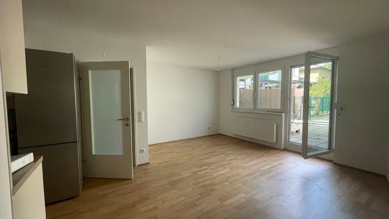 Helles Wohnzimmer mit Parkettboden, großen Fenstern und Zugang zu einem Außenbereich.