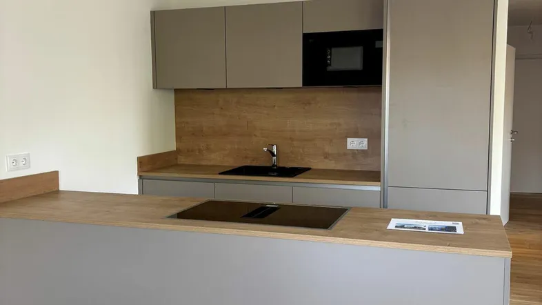 Moderne Küche mit grauen Schränken, Holzarbeitsplatten und integrierten Geräten, inklusive Kochinsel mit Induktionskochfeld.