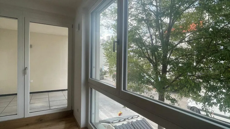 Helles Zimmer mit großen Fenstern, Holzboden und Blick auf die grüne Umgebung.