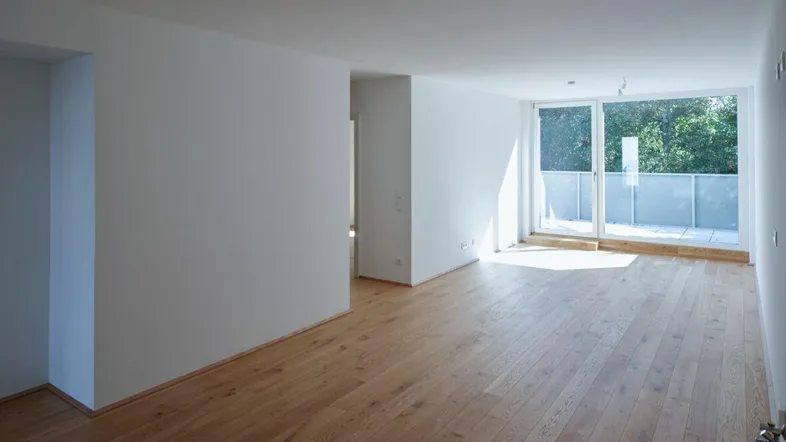 Helles, leeres Zimmer mit Holzboden und Zugang zu einem Balkon, ideal für Wohn- oder Schlafbereich.