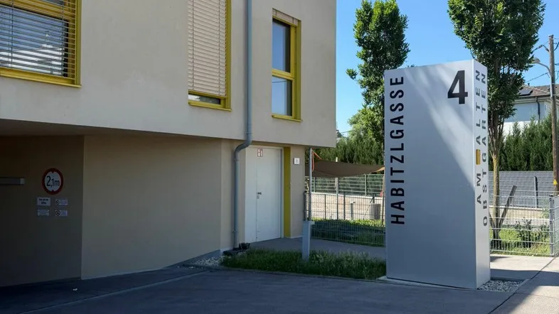 Modernes Gebäude mit gelben Fensterrahmen und einem Hinweisschild zur Adresse.