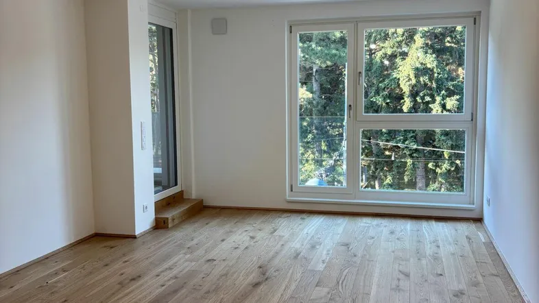 Heller Raum mit neuem Holzboden und großen Fenstern mit Blick ins Grüne.