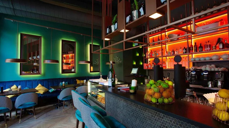 Moderne Bar mit leuchtend grünen Wänden, einer beleuchteten Bar und bequemen Sitzgelegenheiten.
