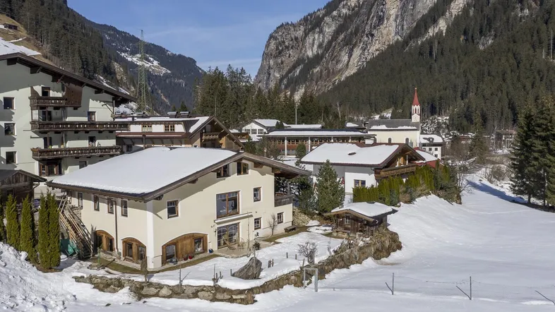 Panoramablick auf ein verschneites Bergdorf mit traditionellen Häusern und majestätischen Bergen im Hintergrund.