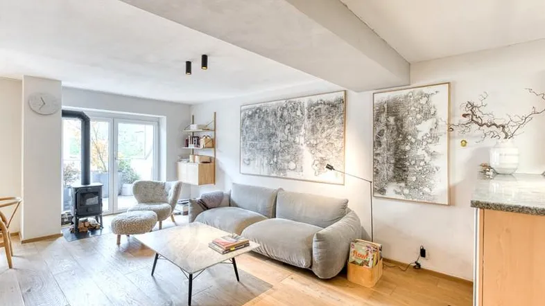 Helles Wohnzimmer mit Holzboden, Kaminofen und Zugang zu einer Außenterrasse.