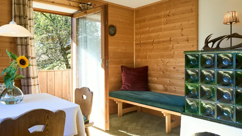 Gemütlicher Essbereich mit traditionellem Kachelofen, Holzwänden und Zugang zum Außenbereich.