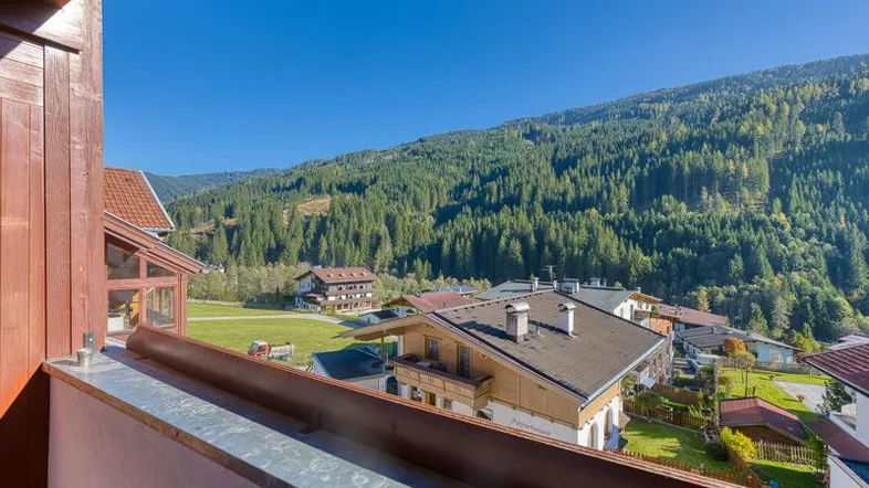 Balkon mit Holzelementen und weitem Blick auf die umliegende Berglandschaft und bewaldete Hänge.