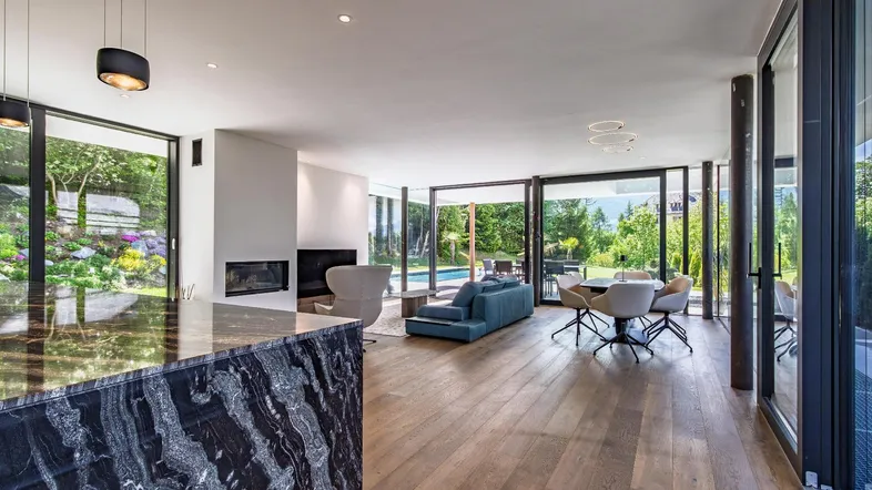Heller, offener Wohn- und Essbereich mit Holzboden, Kamin und Blick auf den Pool und Garten.