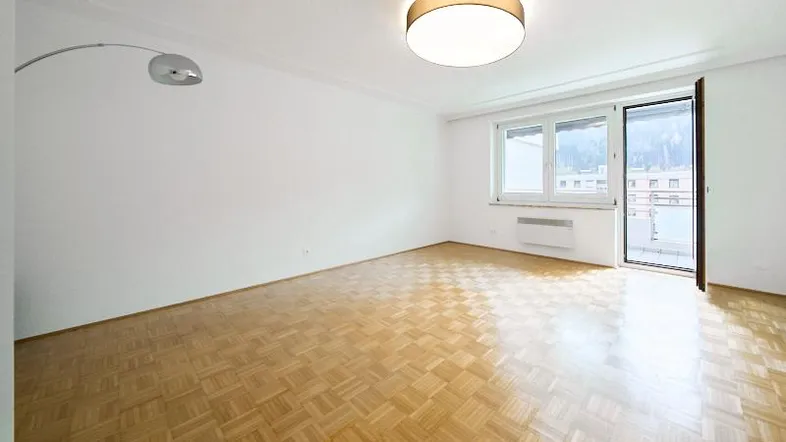 Helles Zimmer mit Parkettboden, weißen Wänden und Zugang zu einem Balkon.
