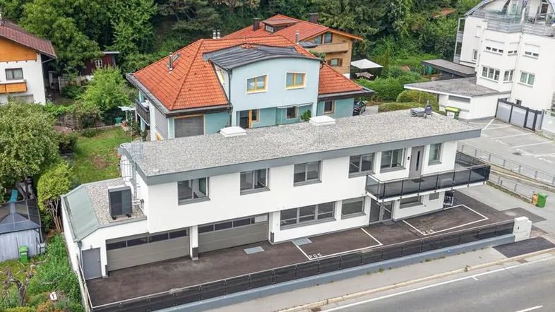 Moderne Wohnanlage mit Flachdach, Garagen im Erdgeschoss und Balkonen, umgeben von Bäumen.