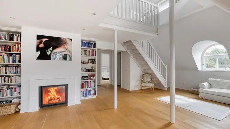 Helles Wohnzimmer mit Kamin, Bücherregalen, Holzfußboden und offener Galerie zum Obergeschoss.
