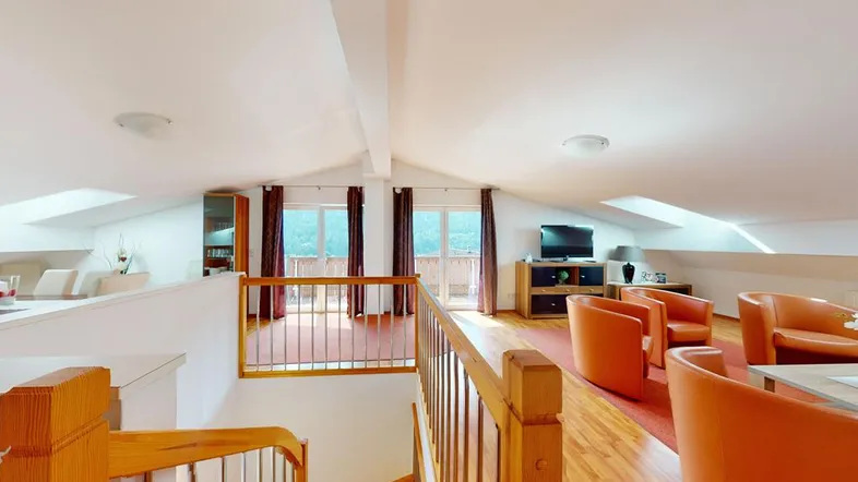 Helles Wohnzimmer im Dachgeschoss mit Holzboden, Dachschrägen und Zugang zum Balkon.