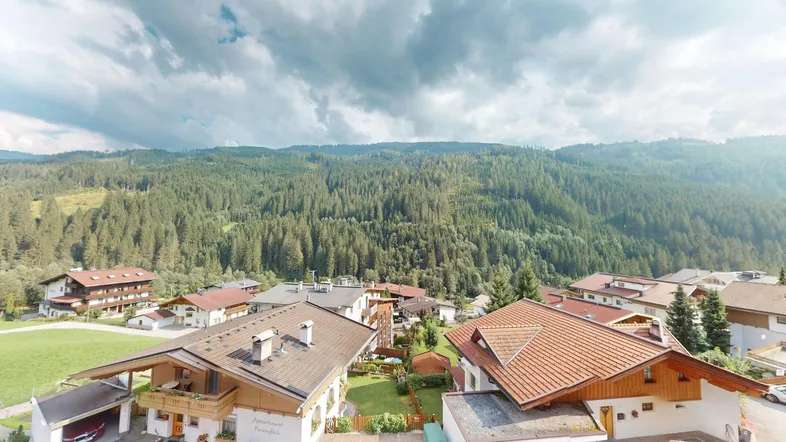 Panoramablick auf die umliegende Berglandschaft mit traditionellen Häusern und dichten Wäldern.
